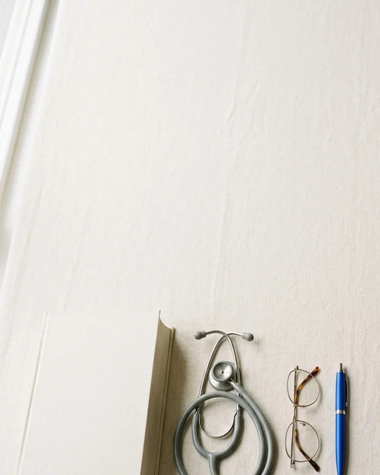 A physician's desk with a reference book, stethoscope, and a cobalt blue pen